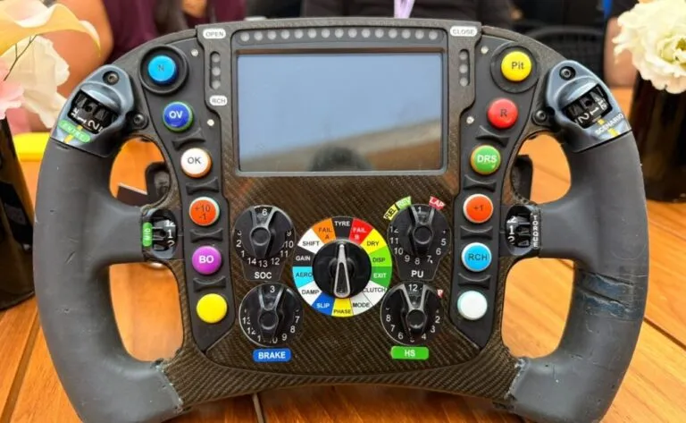 Volante de Fórmula 1 con pantalla digital, botones, perillas y paletas para controlar diferentes funciones del monoplaza.